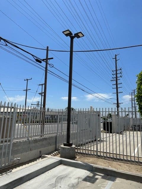 Streetlight near a fenced area with power lines and a blue sky in the background.