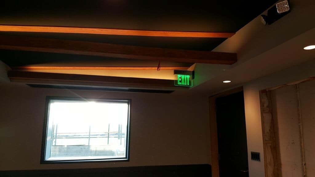 Modern interior room with wooden beam ceiling, bright window, and illuminated exit sign.