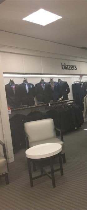 Display of blazers on racks in a clothing store with seating area in foreground.