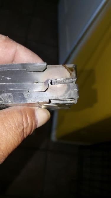 Damaged metal component held in hand, showing dents and wear, with a yellow background.