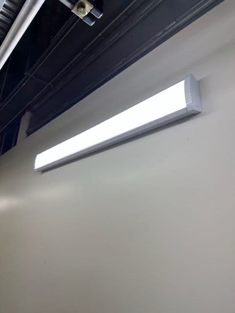 LED ceiling light fixture mounted on a white wall in a commercial space.