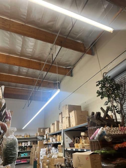Brightly lit warehouse interior with wooden beams, shelves stocked with boxes and decorative items.