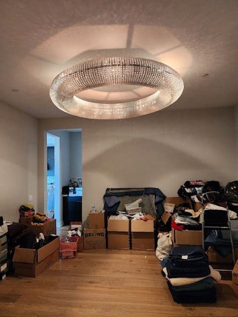 Cluttered room with boxes and clothes beneath a modern chandelier.