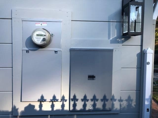 Electrical meter and utility box mounted on a gray wall with a lantern fixture nearby.