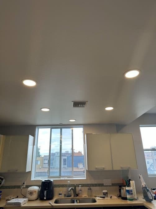 Brightly lit kitchen with recessed ceiling lights and large window for natural light.