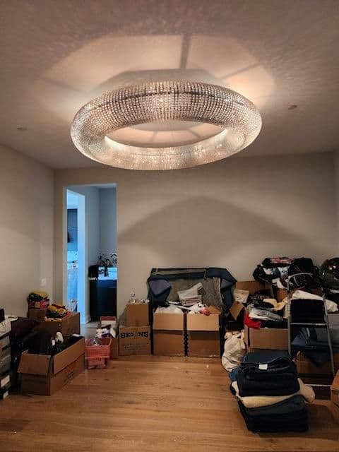 Modern crystal chandelier illuminating a cluttered room with boxes and clothing.