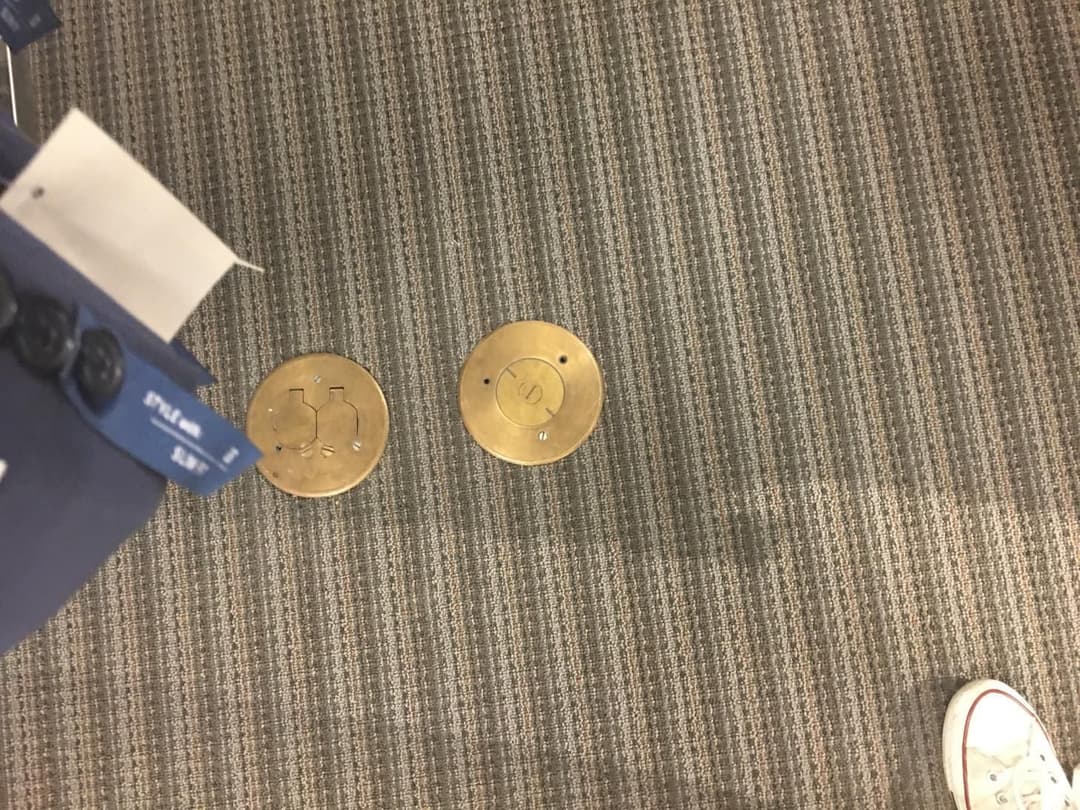 Brass floor plates with electrical symbols on carpeted surface in retail space.