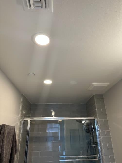 Modern bathroom with recessed lighting and glass shower enclosure. Neutral gray tiles.
