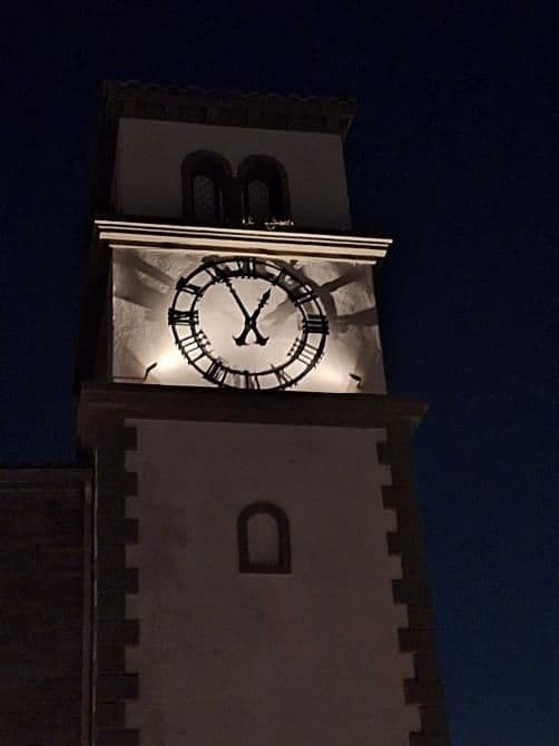 Illuminated clock tower at night, showcasing detailed Roman numerals and elegant architecture.