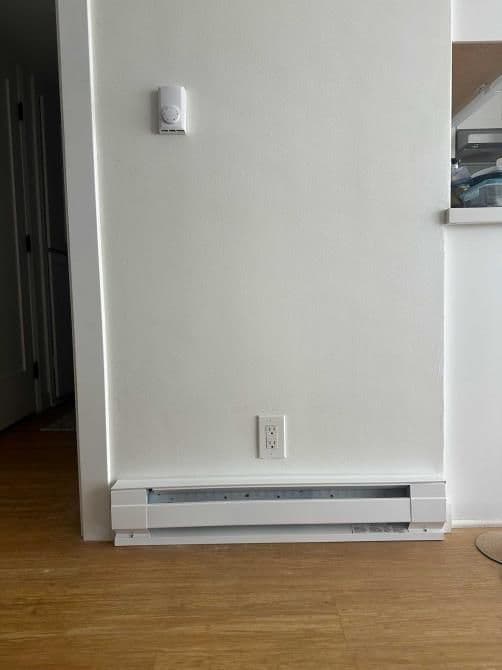 Baseboard heater on a wall in a modern, minimalist interior with light wood flooring.