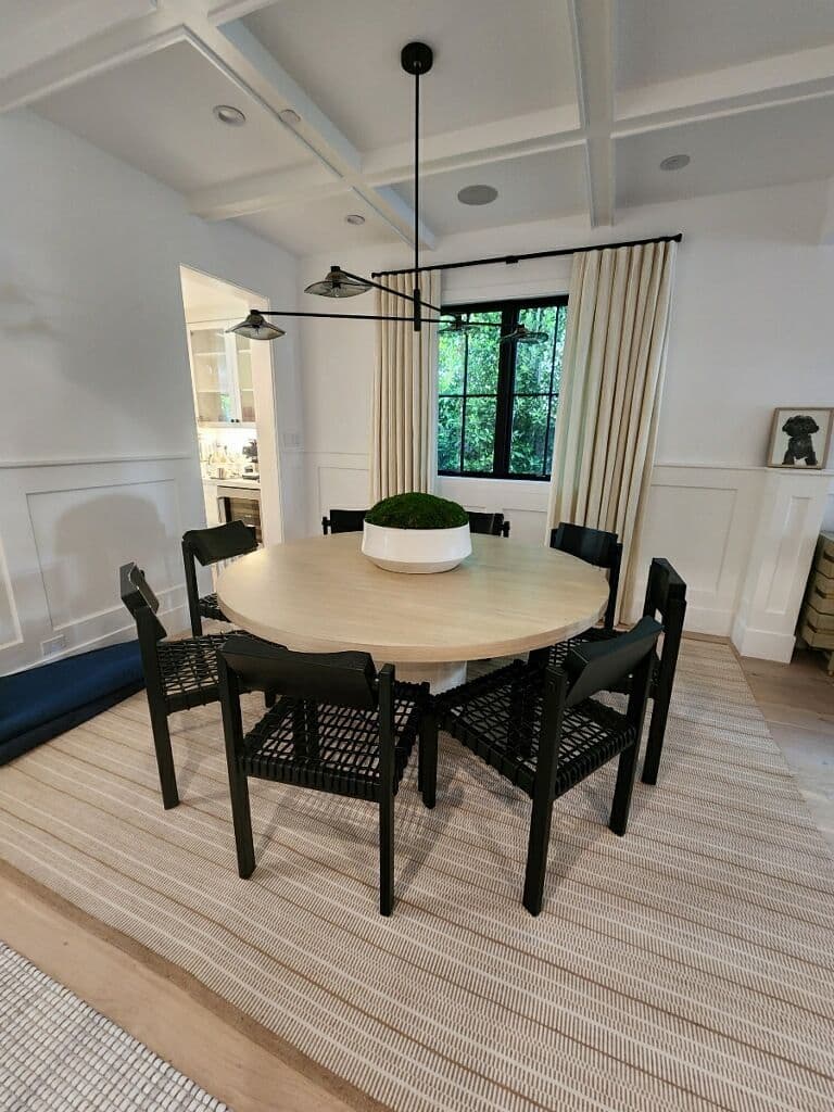 Modern dining room with a round wooden table, black chairs, and natural decor accents.
