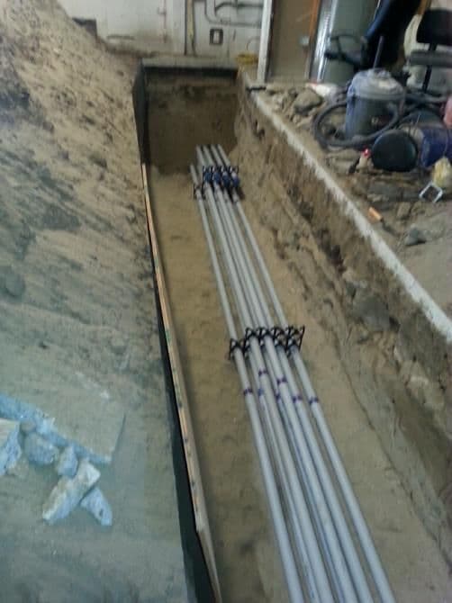 Excavated trench with laid PVC pipes in a construction site.