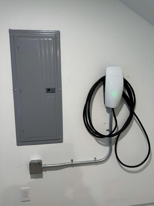 Electric vehicle charger mounted on wall next to electrical panel, showcasing installation details.