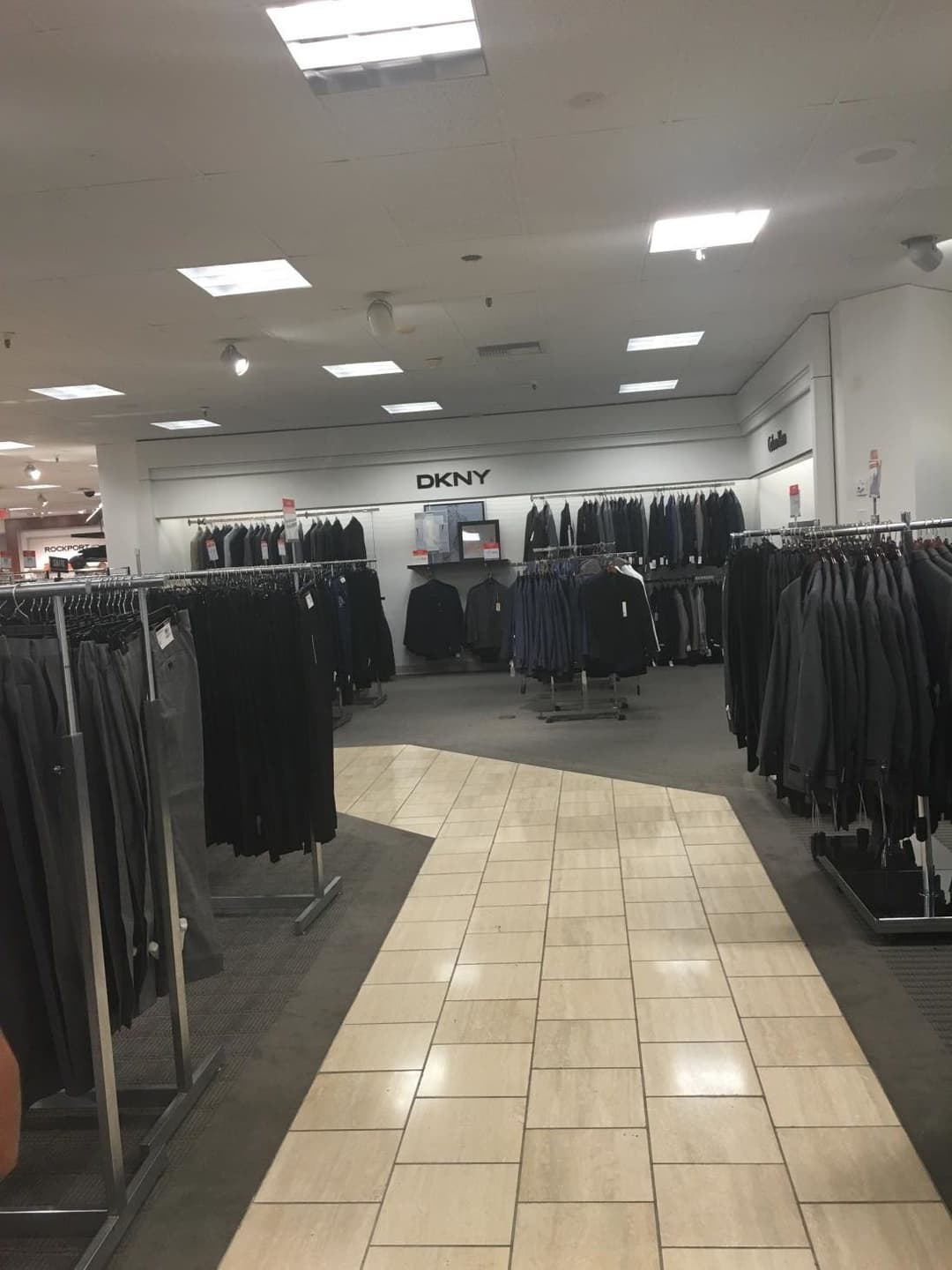 Men's clothing section with DKNY display featuring suits and dress pants on hangers.