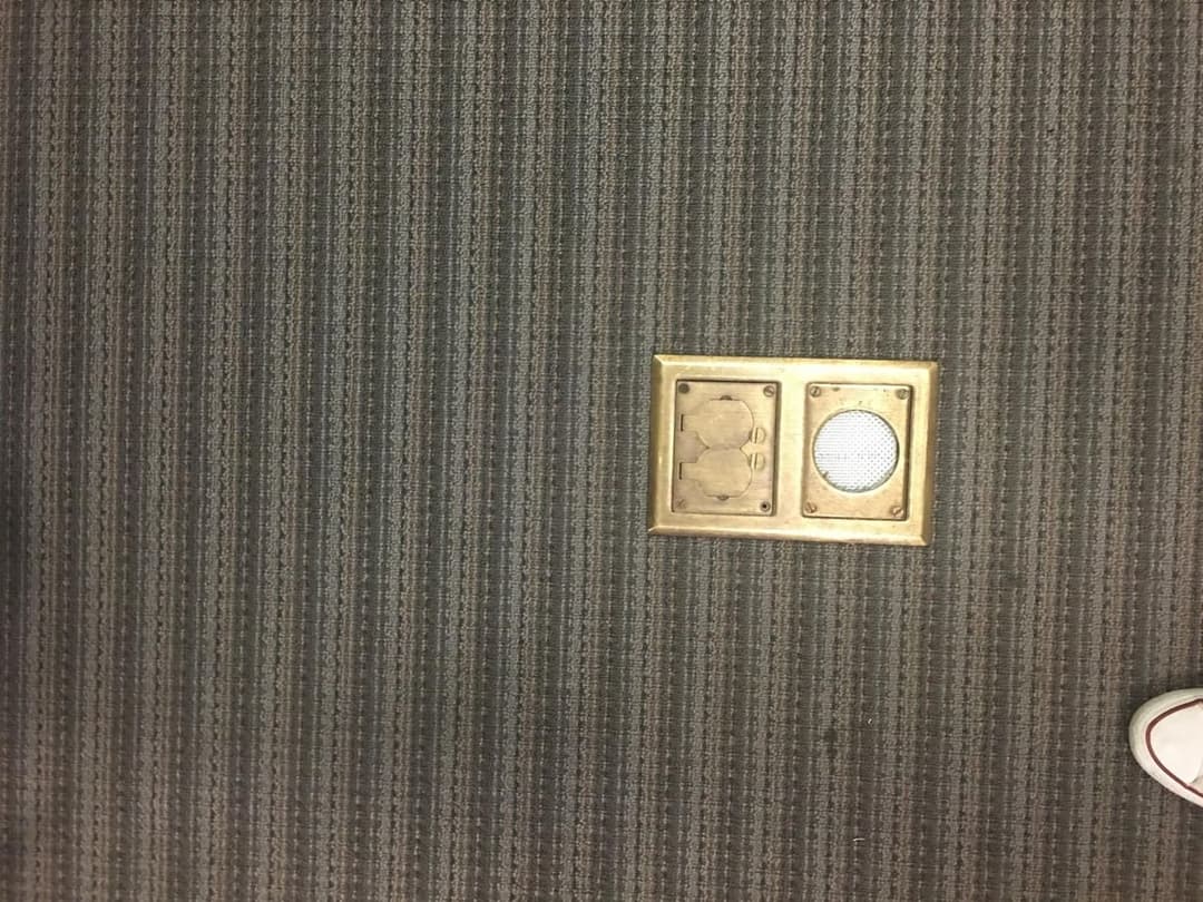 Floor with a metal vent cover on a gray striped carpet. Foot partially visible.