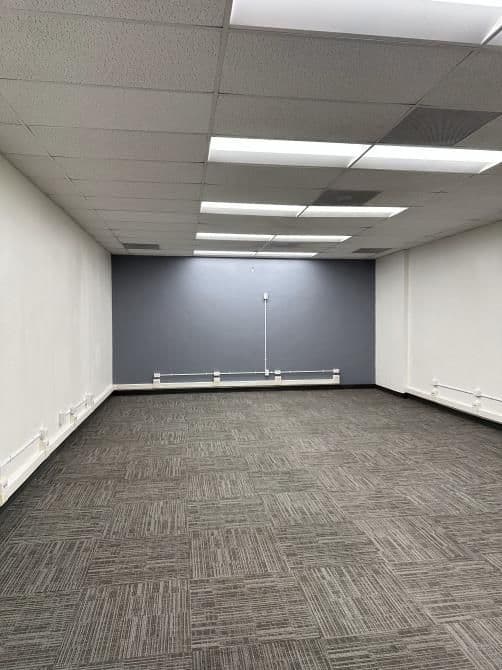 Empty office space with gray walls and patterned carpet, well-lit by ceiling lights.