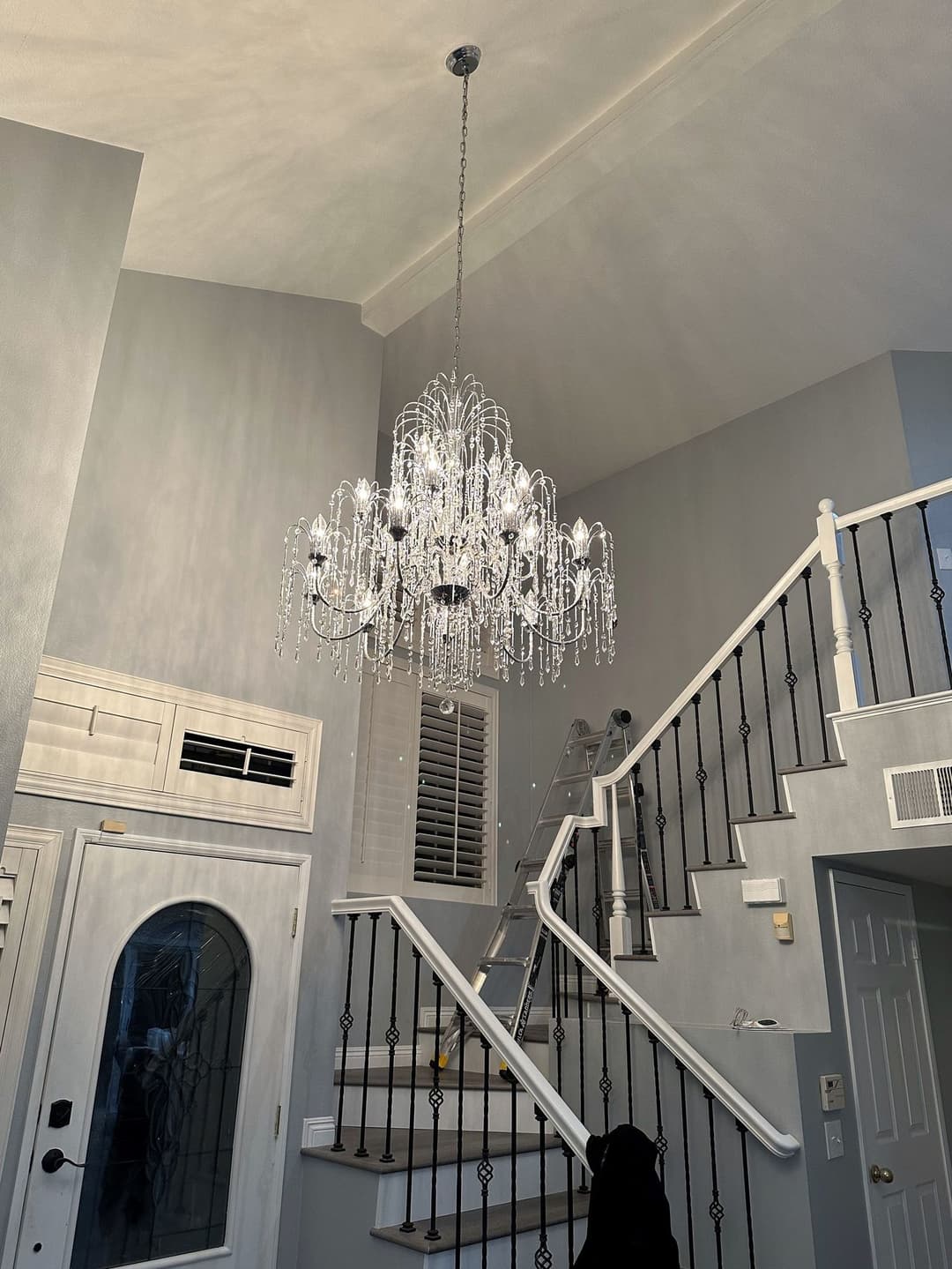 Elegant crystal chandelier suspended in a modern foyer with a staircase and light gray walls.