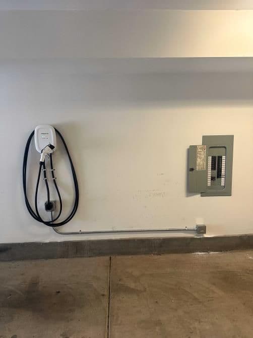 Electric vehicle charger mounted on wall near electrical panel in a garage setting.